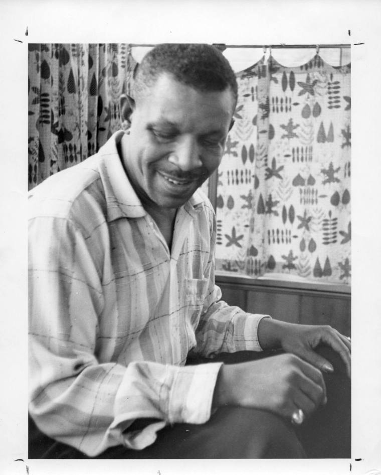 Black and white photo of Al Hibbler sitting  with his hands resting on his knees. 